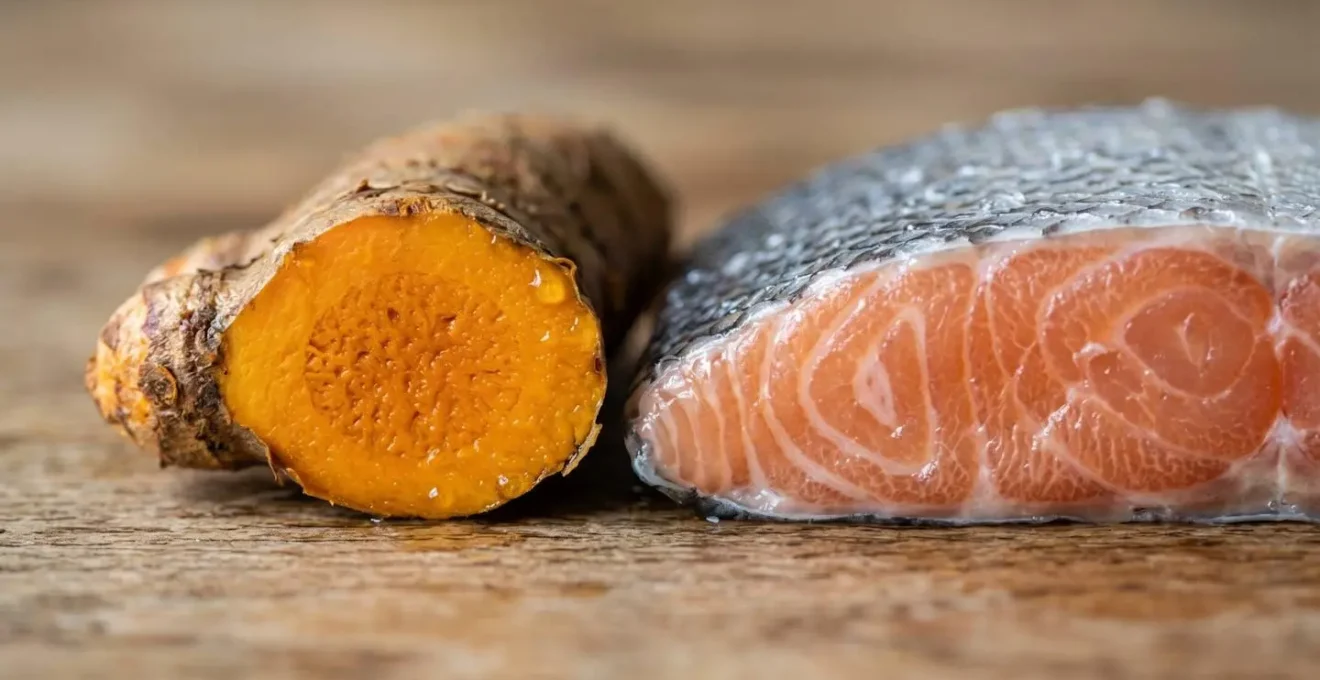 Artistic macro close-up of omega-3 rich fish and vibrant turmeric root on a natural wooden surface showing rich textures and complementary colors in warm natural lighting