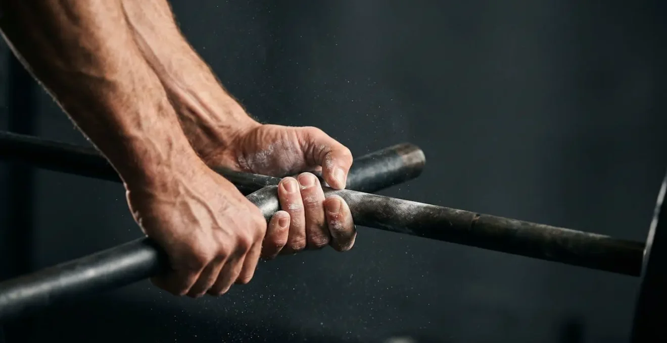 Close-up of hands gripping a barbell with chalk dust suspended in dramatic lighting showing muscle engagement